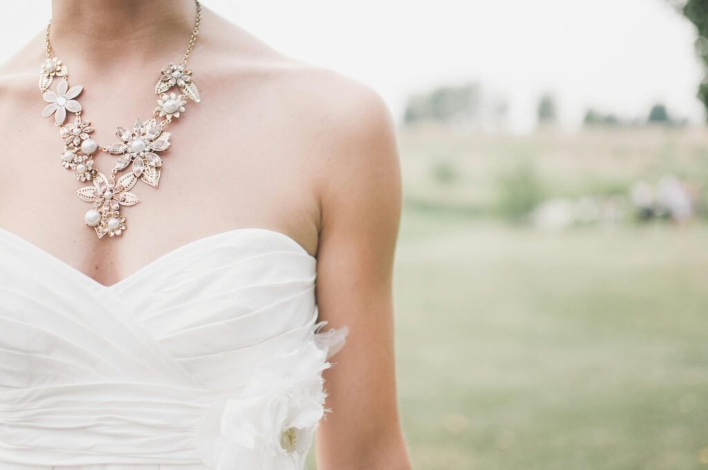 Close-up of a floral necklace adorning a bride in a strapless white wedding dress outdoors.